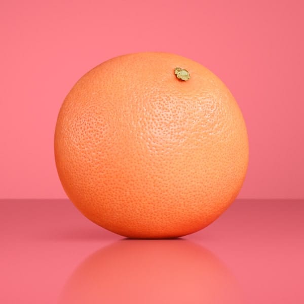 One full grapefruit on a pink background