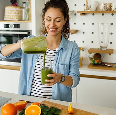 Young woman pouring a smoothie with citrus on the counter